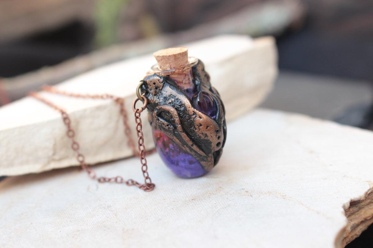 lchemist-inspired pendant with a purple potion bottle and intricate bronze details