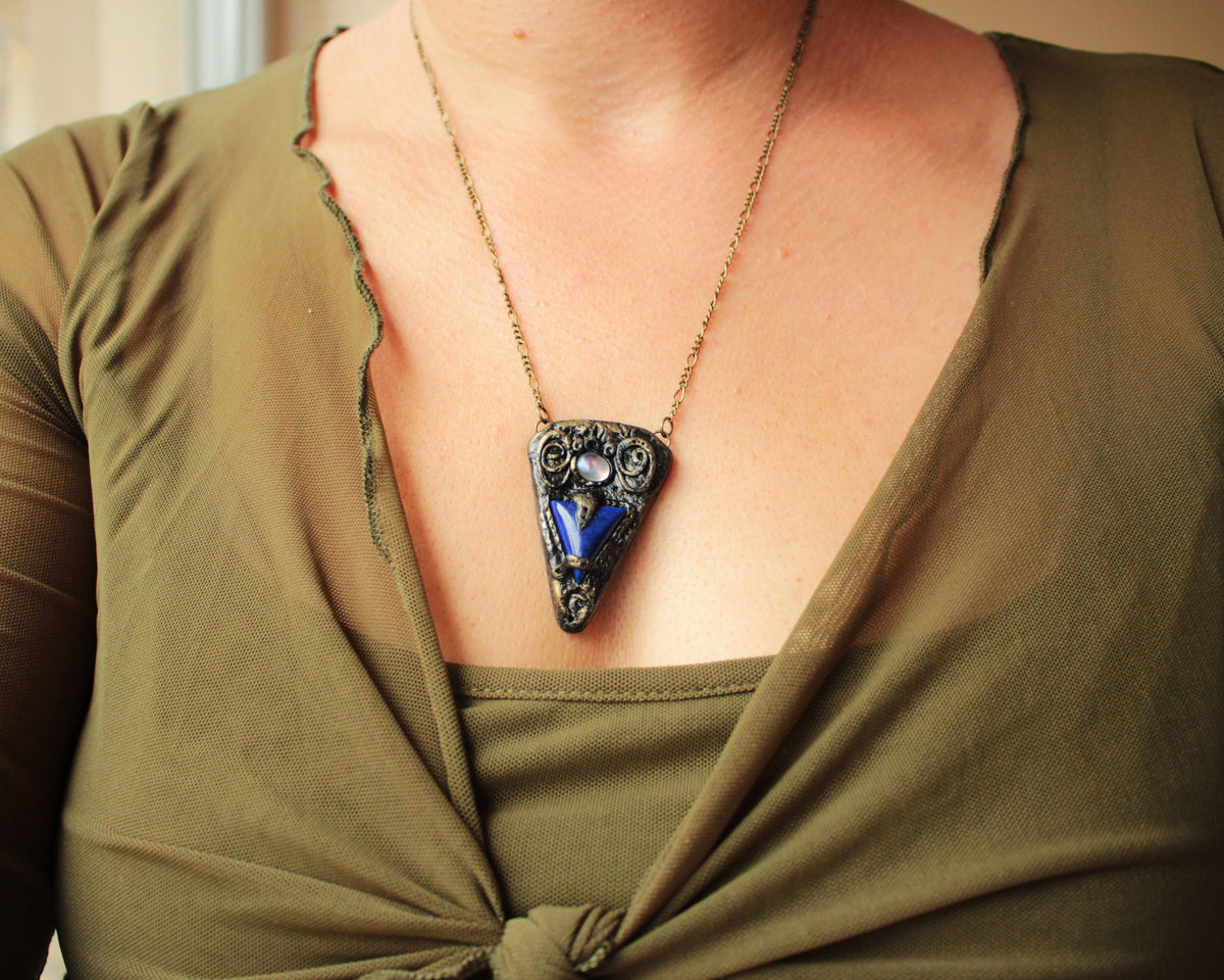 Ancient-inspired talisman jewelry with a blue gemstone and textured metallic finish