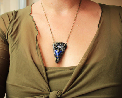 Ancient-inspired talisman jewelry with a blue gemstone and textured metallic finish