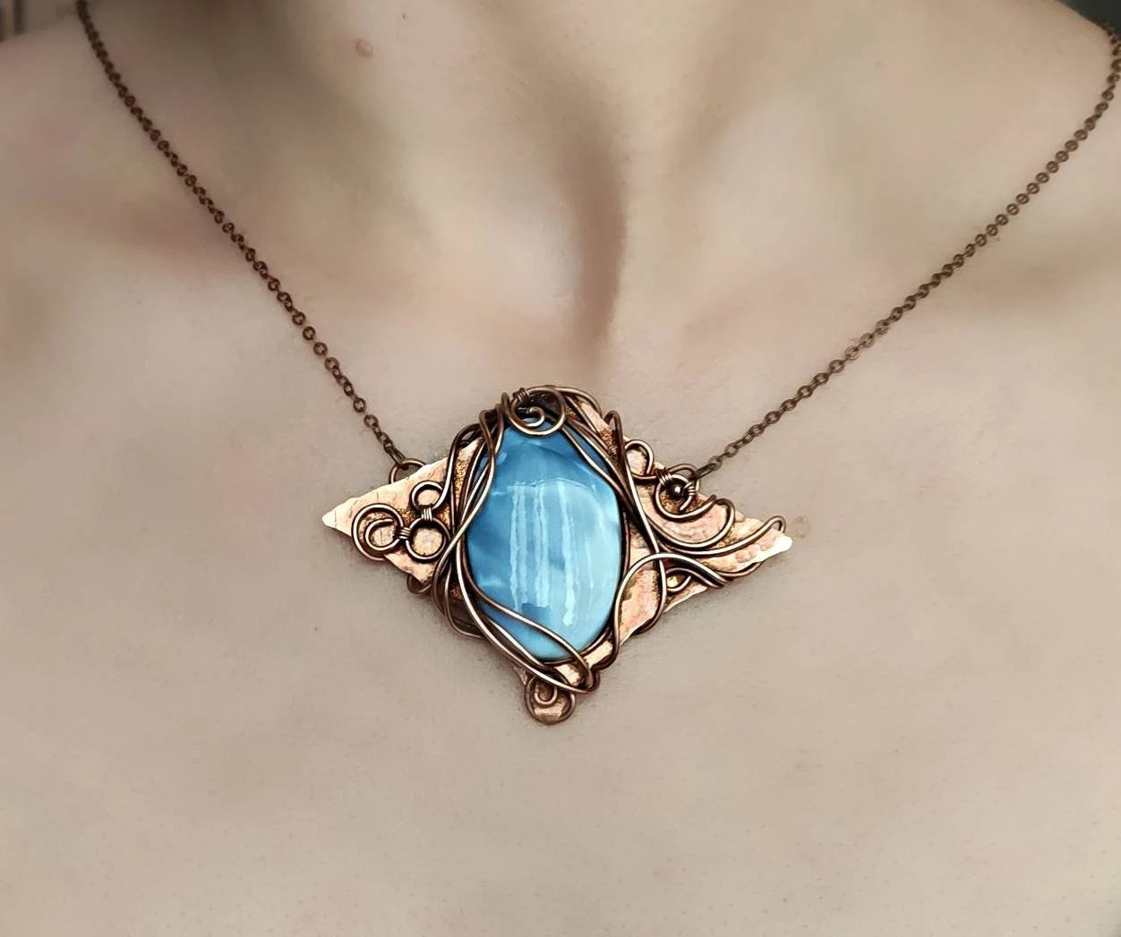 Close-up of handmade copper pendant featuring shimmering blue opal gemstone