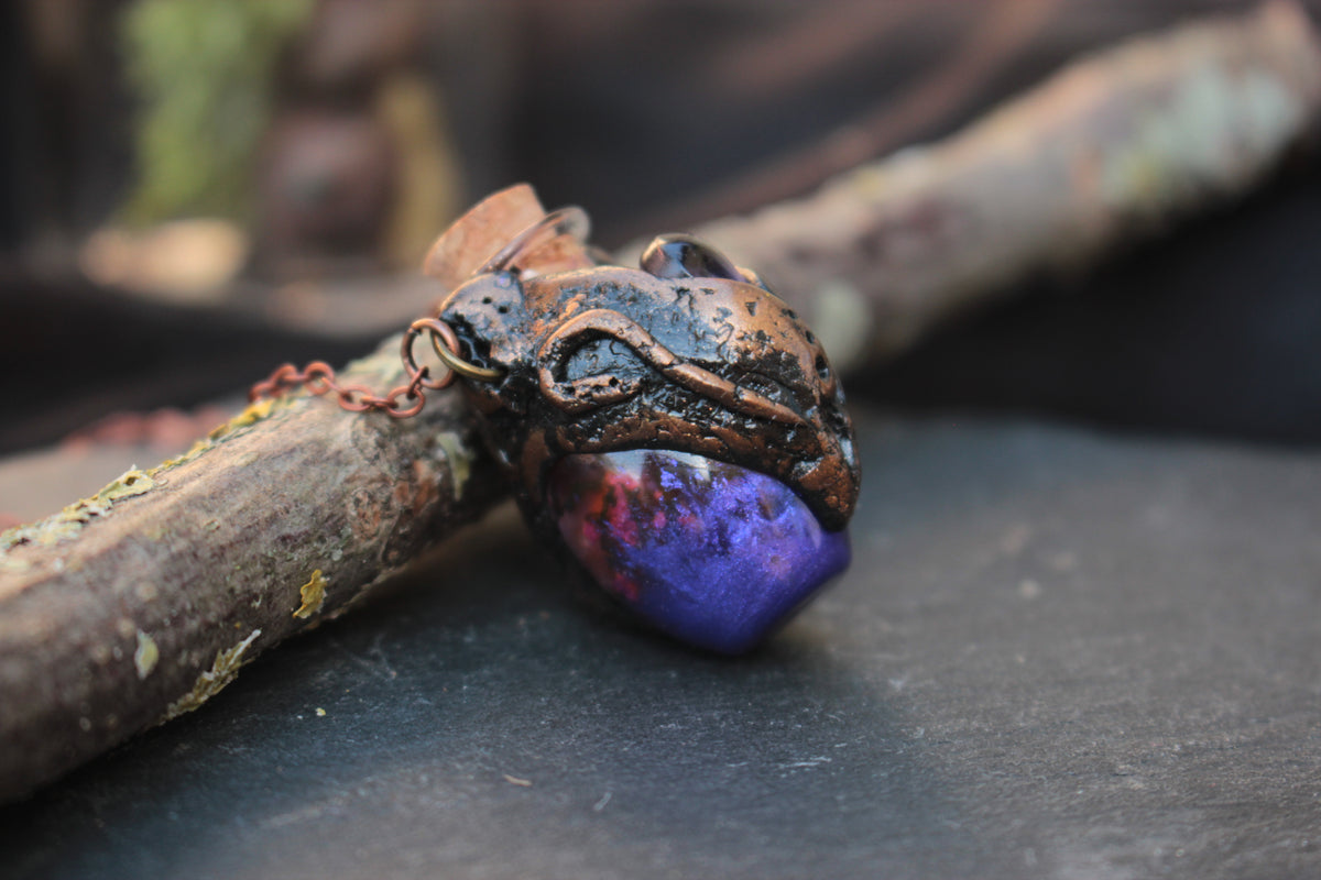 Bronze-toned fantasy pendant with a small purple potion bottle