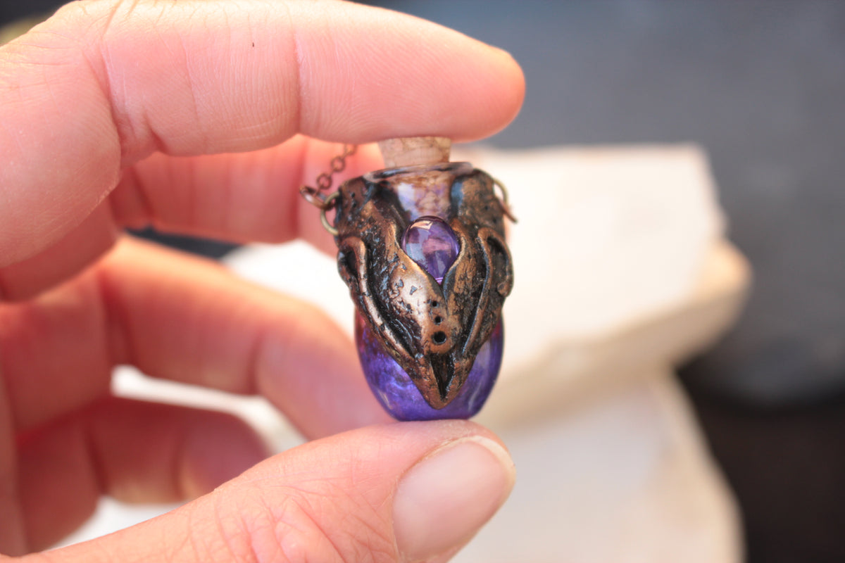 Dark fantasy pendant necklace with a deep violet potion and antique bronze accents