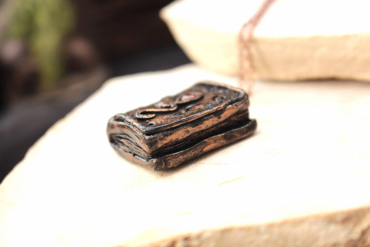 Enchanted book pendant necklace with a small red gemstone