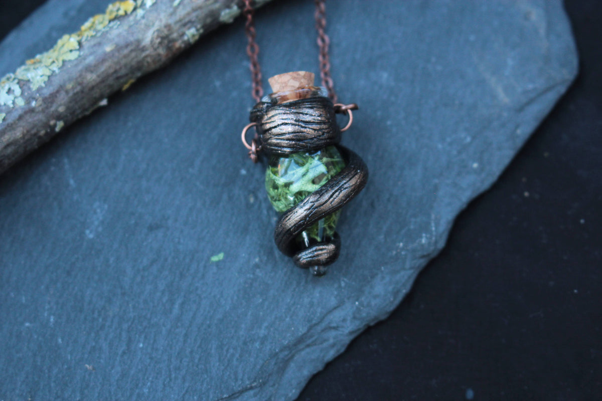 Close-up view of an enchanted-style green vial pendant on a rustic forest branch