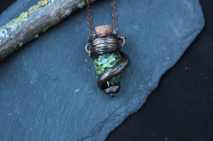 Close-up view of an enchanted-style green vial pendant on a rustic forest branch