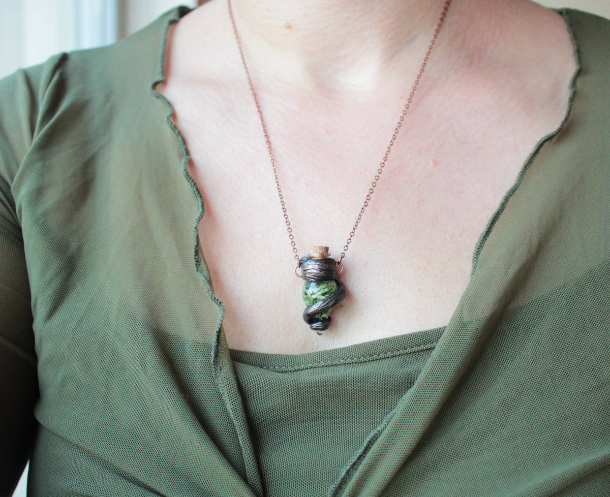 Green fantasy pendant with a small glass vial and twisted branch design
