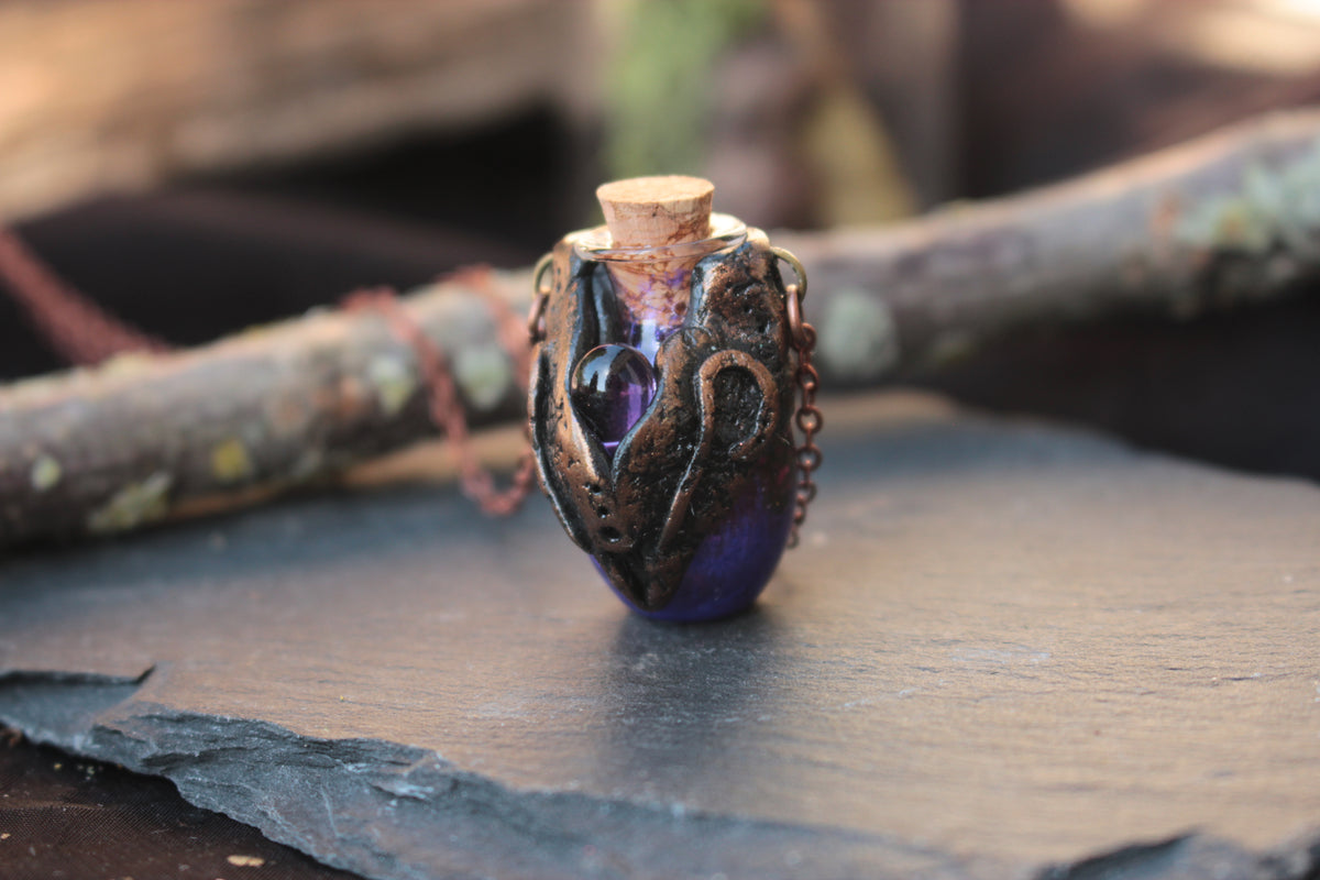 Enchanted fantasy amulet with a violet potion vial and decorative bronze frame