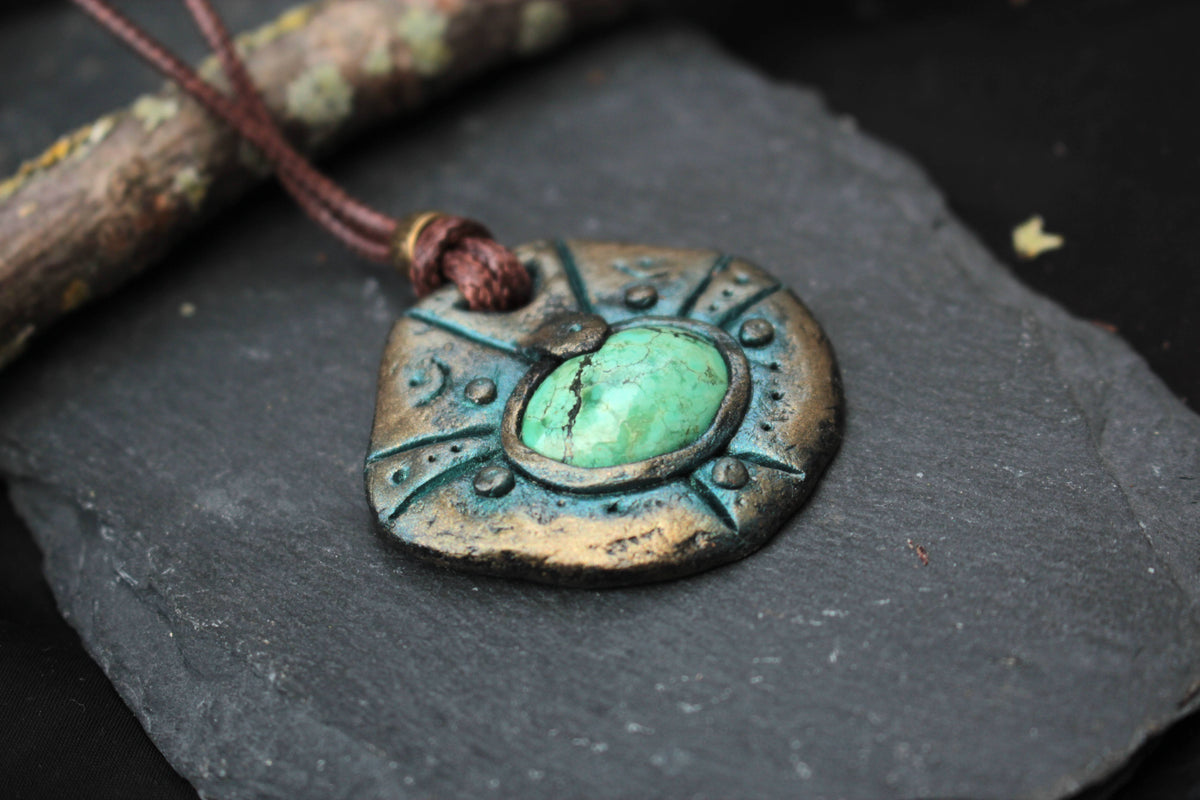 Ancient ruins inspired amulet with an aged metallic finish and green centerpiece