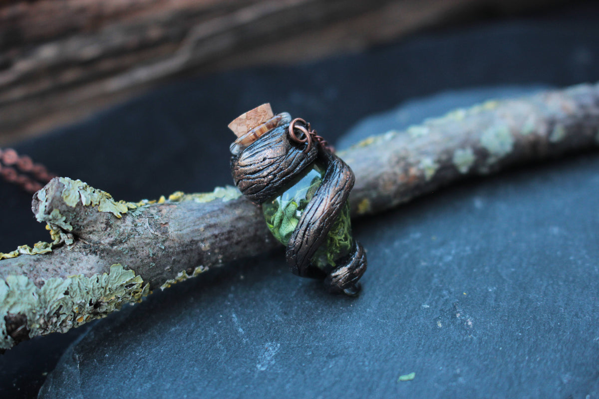 Close-up of a green glass vial pendant wrapped in dark textured vines