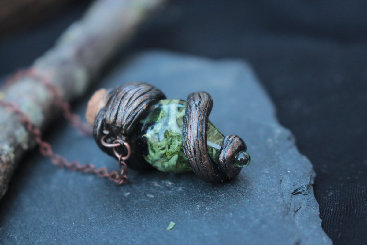 Detailed handmade pendant featuring a green vial surrounded by twisted woodland branches
