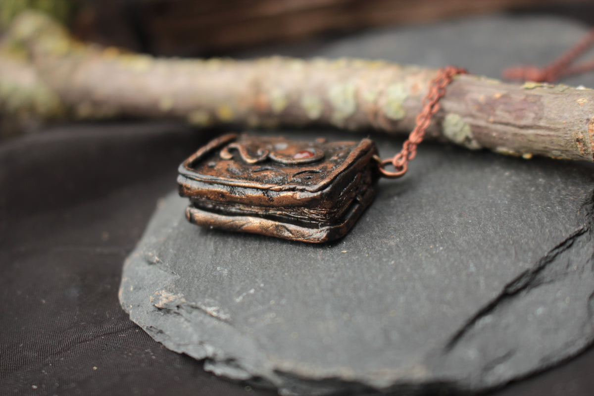 Handmade miniature magic book jewelry with metallic details and gemstone
