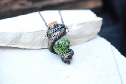 Close-up of a rustic green vial necklace with woodland textures and copper-colored chain